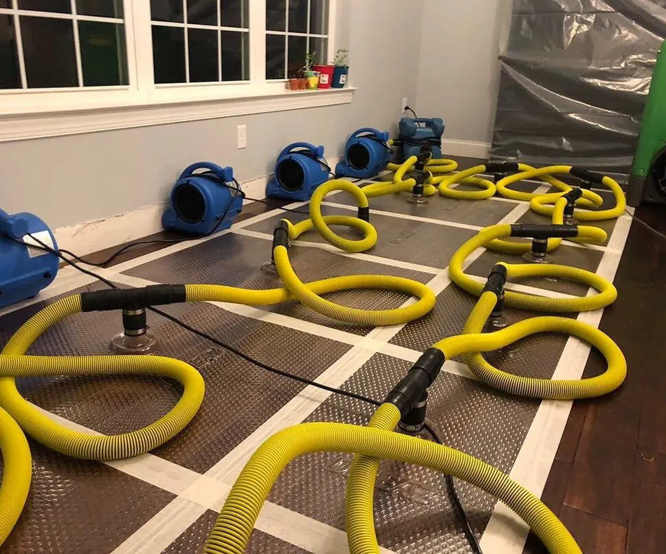 Water damage restoration in Austin — air movers and floor drying mats on a flooded hardwood floor